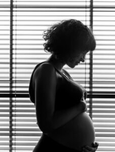 imagen de mujer embarazada en blanco y negro, tocándose la tripa con cara seria.