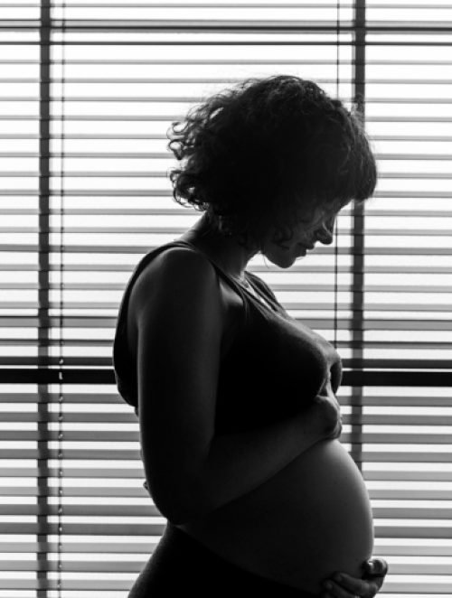 imagen de mujer embarazada en blanco y negro, tocándose la tripa con cara seria.